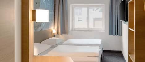 Ein Hotelzimmer mit zwei Betten, einem Schreibtisch, einem Fernseher und einem Fenster mit Vorhängen.