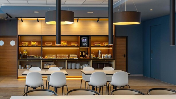 Un comedor moderno con mesas y sillas blancas, una barra de buffet con exhibiciones de comida e iluminación colgante.