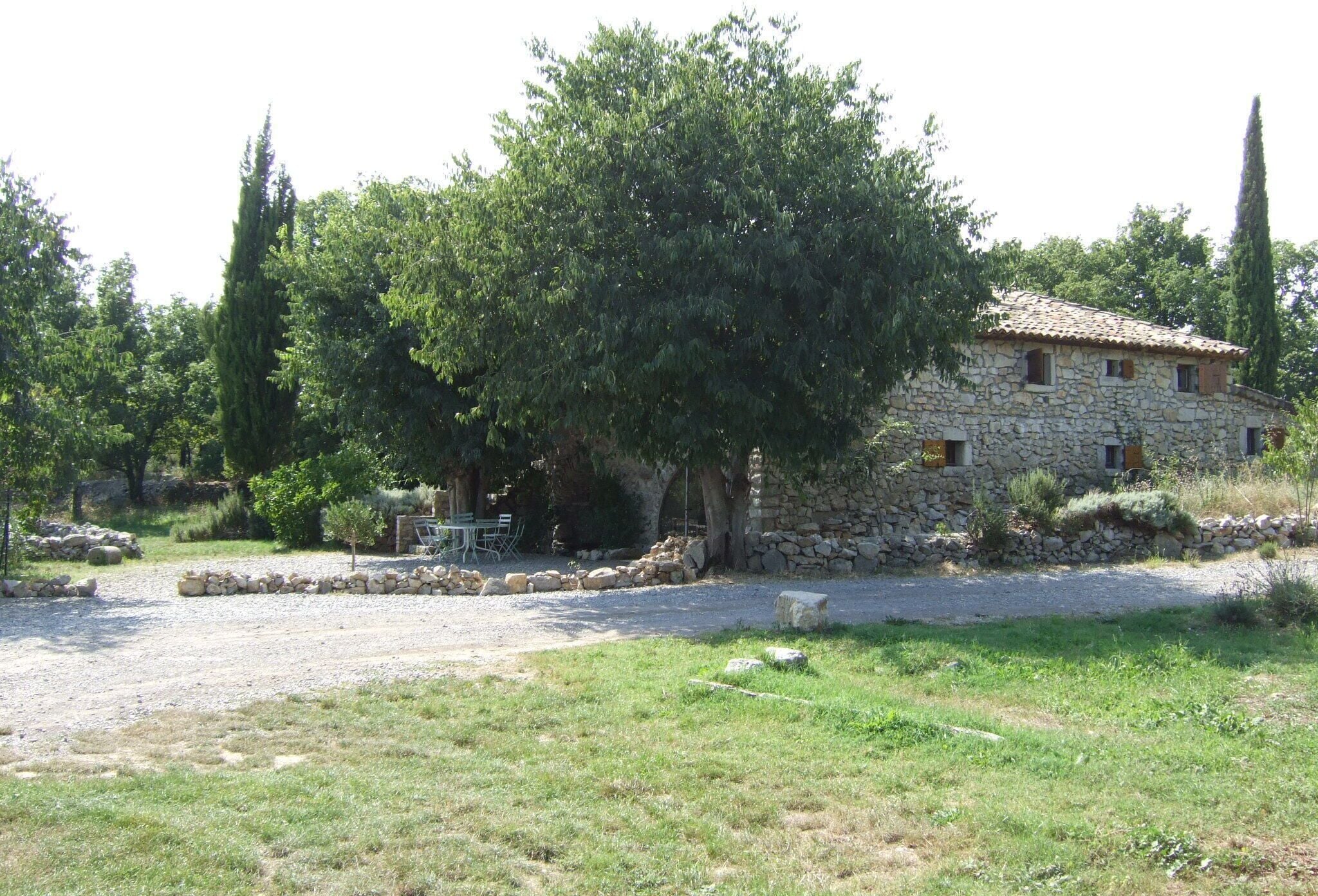A stone building with a tiled roof, surrounded by a gravel driveway and a grassy area.