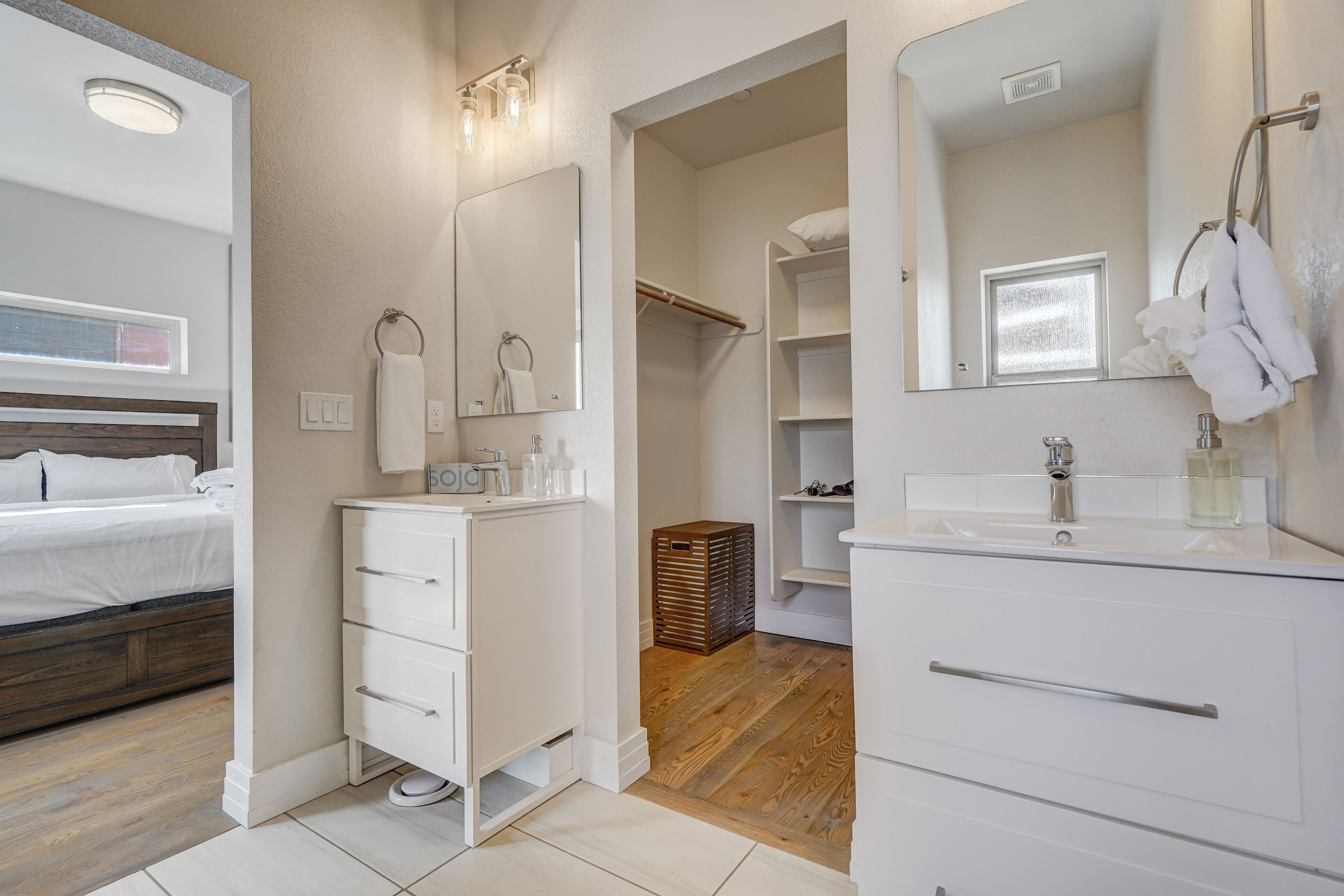 A modern bathroom with a large mirror, white cabinetry, and a wooden floor.