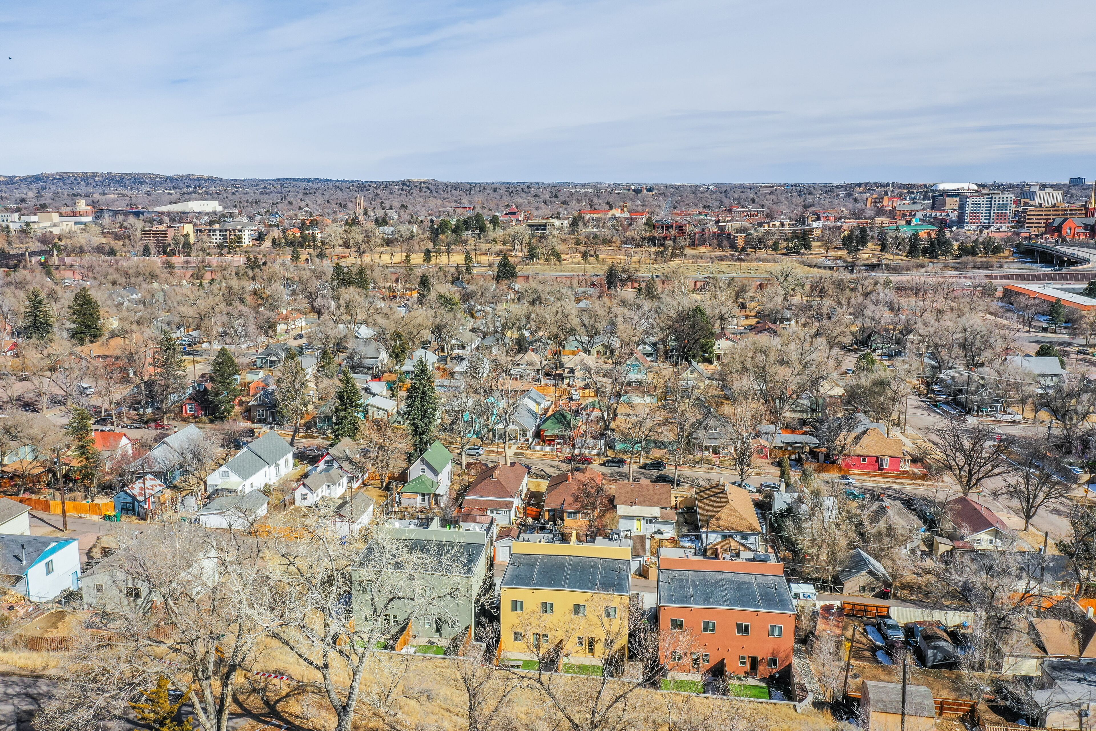 A residential area with houses and buildings, surrounded by trees and hills in the background.