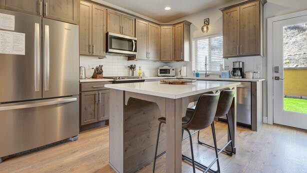 A modern kitchen with stainless steel appliances, wooden cabinets, and a central island with bar stools. - Chipmunk Father Dave (Colorado Springs)
