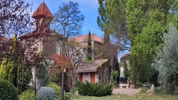 A traditional building with a red-tiled roof and a tower, surrounded by lush greenery and a well-maintained garden. - Spacious holiday home with private pool and park (Puisserguier)