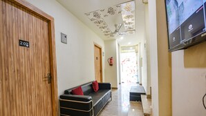 A hallway with a wooden door labeled "202", a black leather sofa with red cushions, a fire extinguisher, and a television mounted on the wall. - FabExpress Divya Villa (New Delhi)