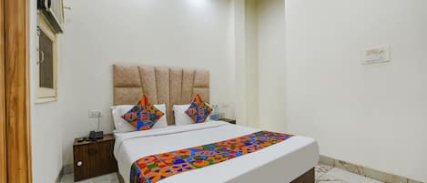 Una habitación de hotel con cama, mesita de noche y aire acondicionado de pared.