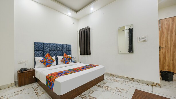 A bedroom with a bed, a nightstand, a wooden door, a mirror, and a bathroom door. - FabExpress Divya Villa (New Delhi)