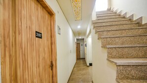 A hallway with a wooden door labeled 207, a staircase with granite steps, and a light fixture on the ceiling. - FabExpress Divya Villa (New Delhi)