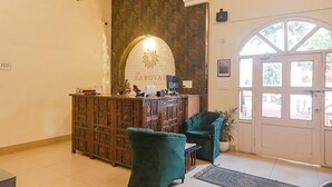 A reception area with a wooden desk, a green armchair, and a large arched doorway. - Fabhotel Sarovar Palace (Prayagraj)