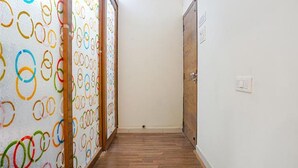 Ein schmaler Flur mit Holzdielen und einer Tür rechts. An der linken Wand befindet sich ein farbenfrohes, kreisförmiges Muster.