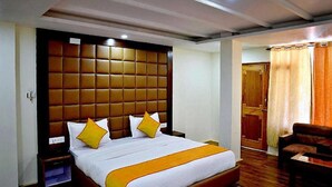 A hotel room with a large bed, a wooden headboard, and a small seating area with a chair and table. - Fabhotel Whistling Winds (Manali)