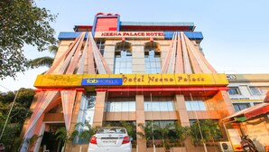 The exterior of Neena Palace Hotel with a prominent sign, a parked car, and a motorcycle.
