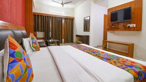 A hotel room with a bed, a television mounted on the wall, a ceiling fan, and a window with curtains.