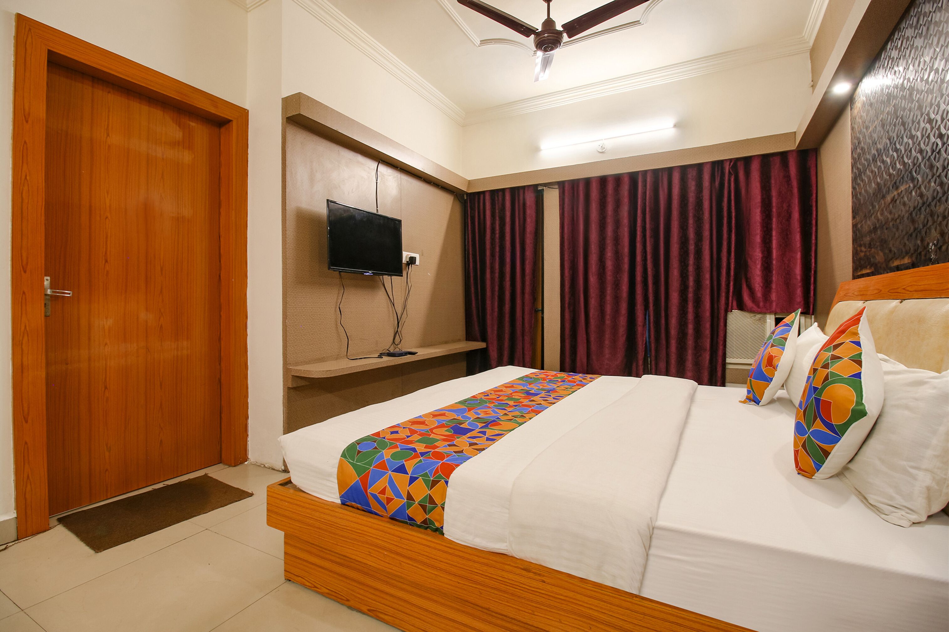 A hotel room with a wooden bed, a television mounted on the wall, and a ceiling fan.