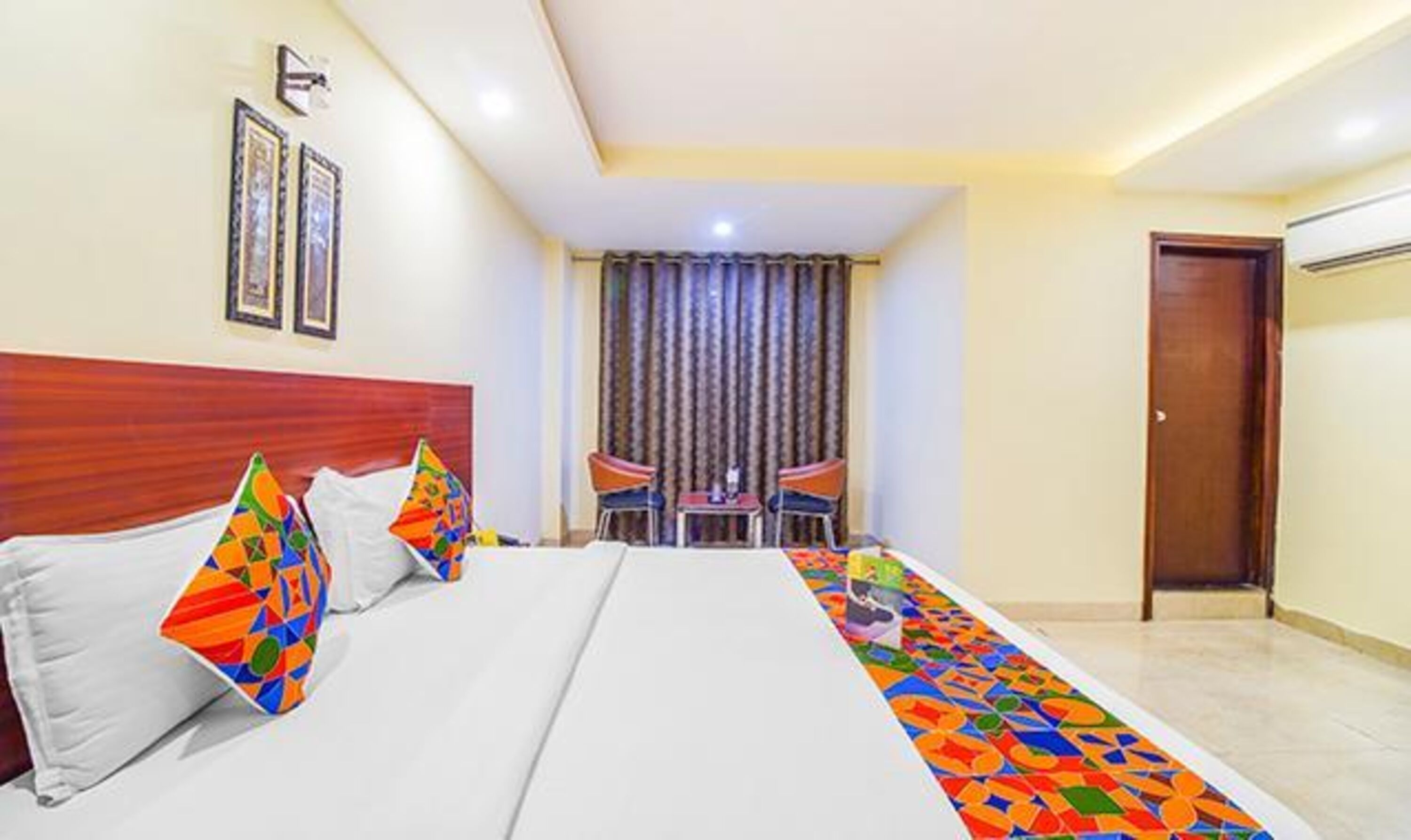A hotel room with a bed, two chairs, a small table, and a door.