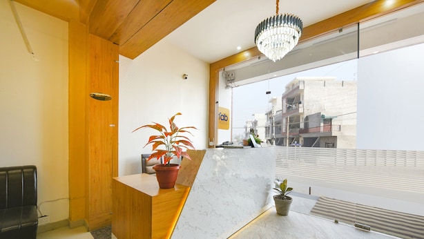 Zona de recepción con mostrador de madera, una planta en maceta y vistas a edificios a través del ventanal.