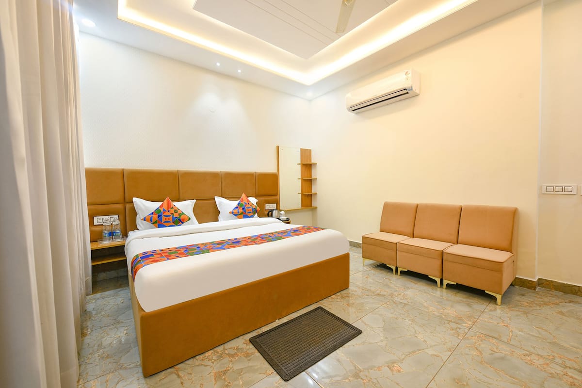A hotel room with a bed, a sofa, a bedside table, an air conditioner, and a ceiling light.