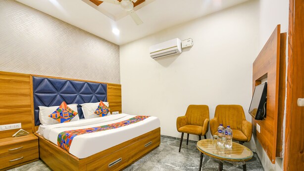 Una habitación de hotel con una cama de madera, dos sillones, una mesita con botellas de agua, un equipo de aire acondicionado y un televisor montado en la pared.