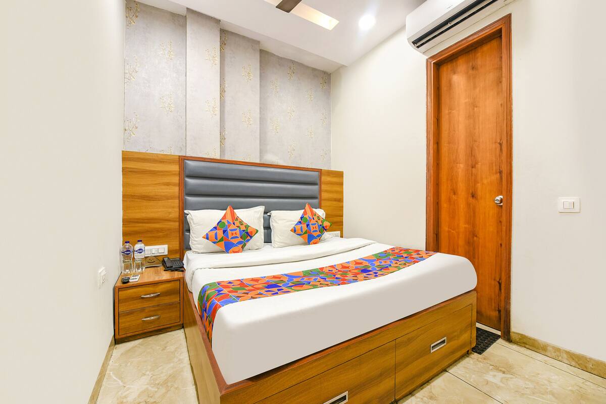 A neatly made bed with a patterned bedspread, a wooden headboard, and a nightstand with a phone and water bottles.