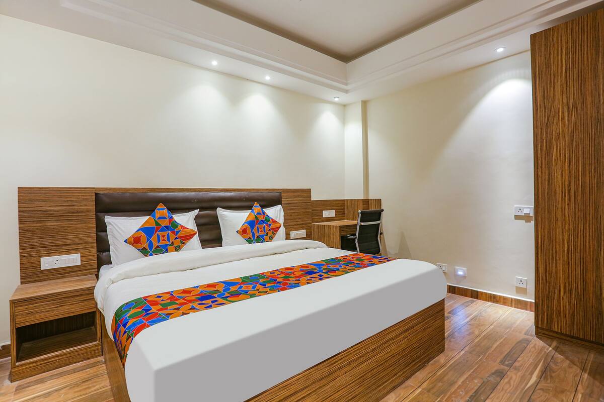 A modern hotel room with a large bed, wooden headboard, and a colorful geometric-patterned bedspread.