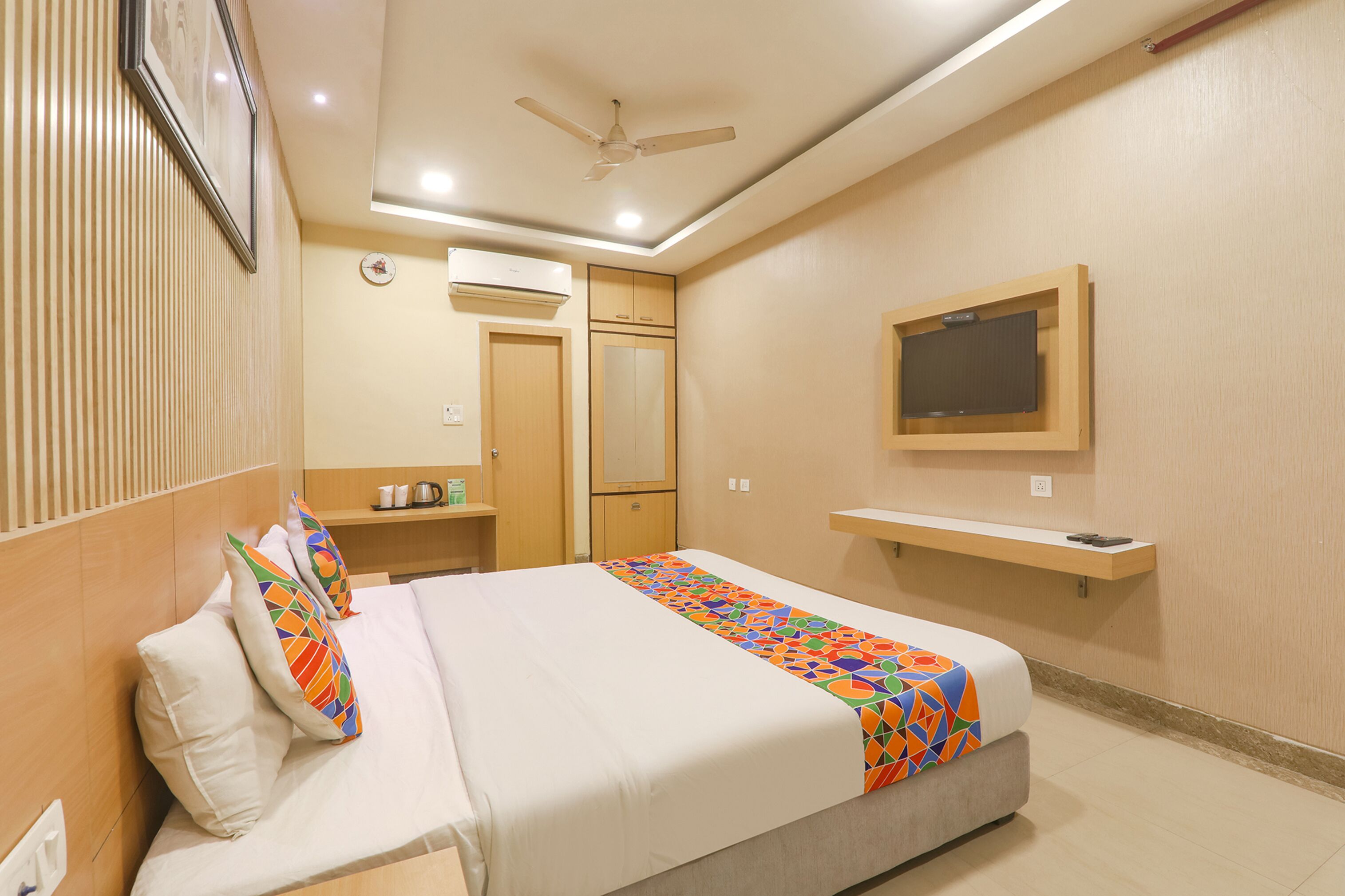 Habitación de hotel con cama, ventilador de techo, televisor montado, estante y armario.