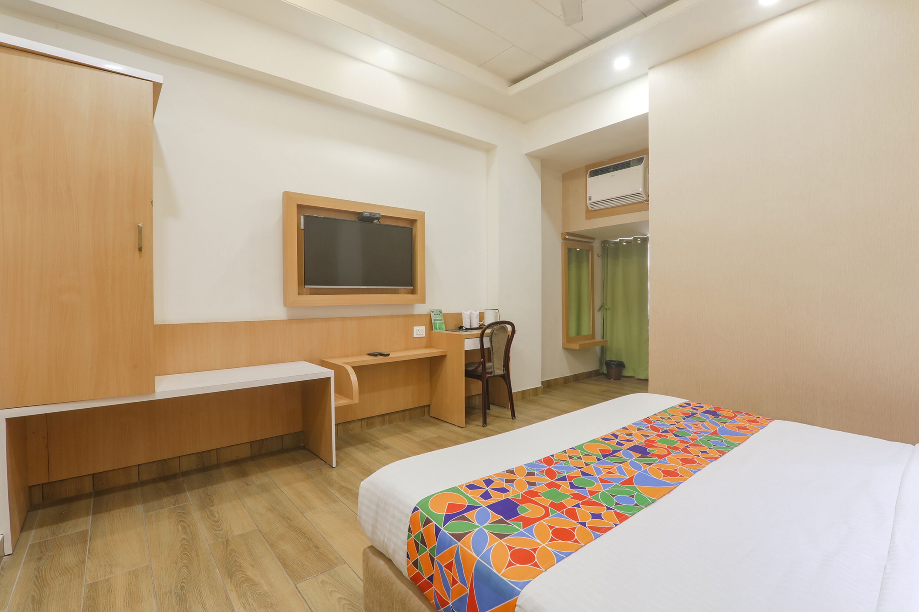 A hotel room with a bed, a desk, a chair, a wardrobe, and an air conditioning unit.