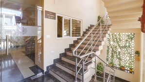 Un escalier avec des rampes en métal, une entrée avec une porte en verre et un mur orné d’un panneau végétal décoratif.