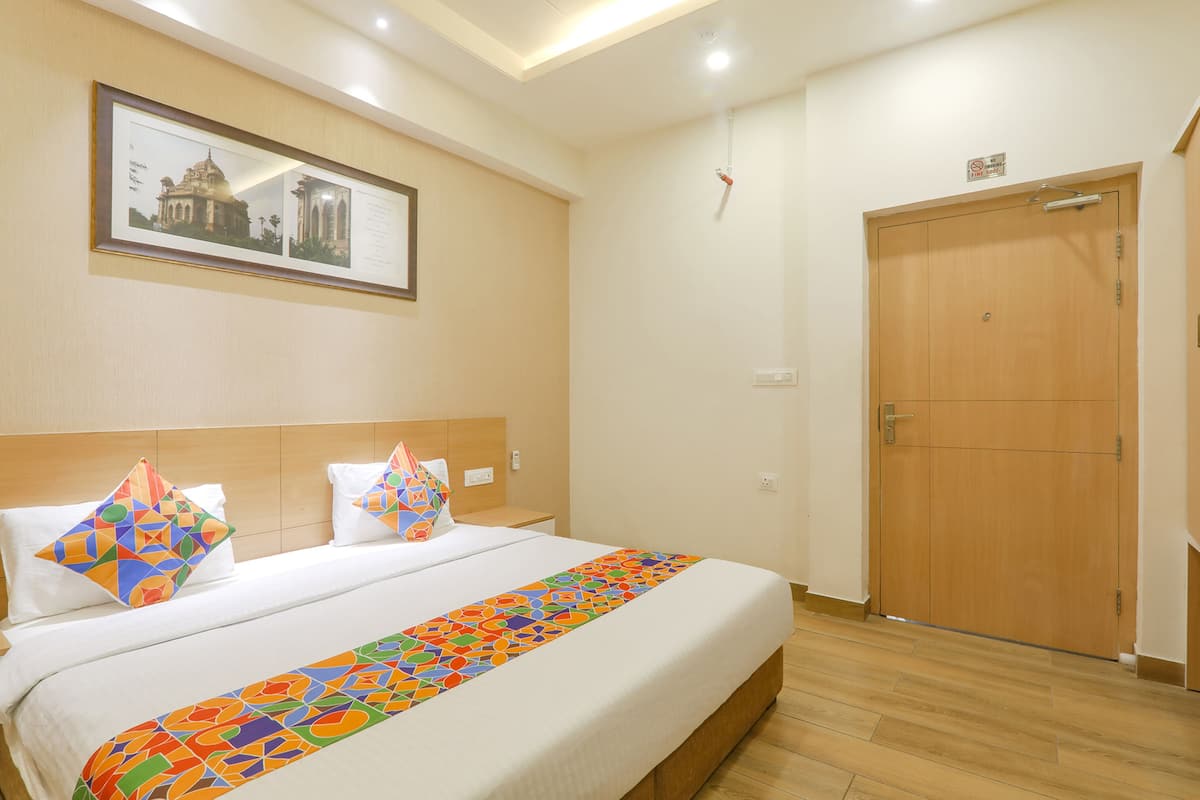 Habitación de hotel con una cama grande, un cuadro en la pared, una puerta de madera y un pequeño letrero encima de la puerta.