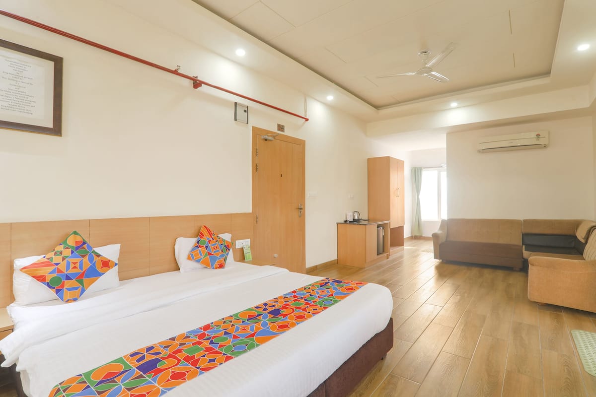 Habitación de hotel con una cama grande, cabecera de madera, escritorio con silla, sofá y equipo de aire acondicionado en la pared.