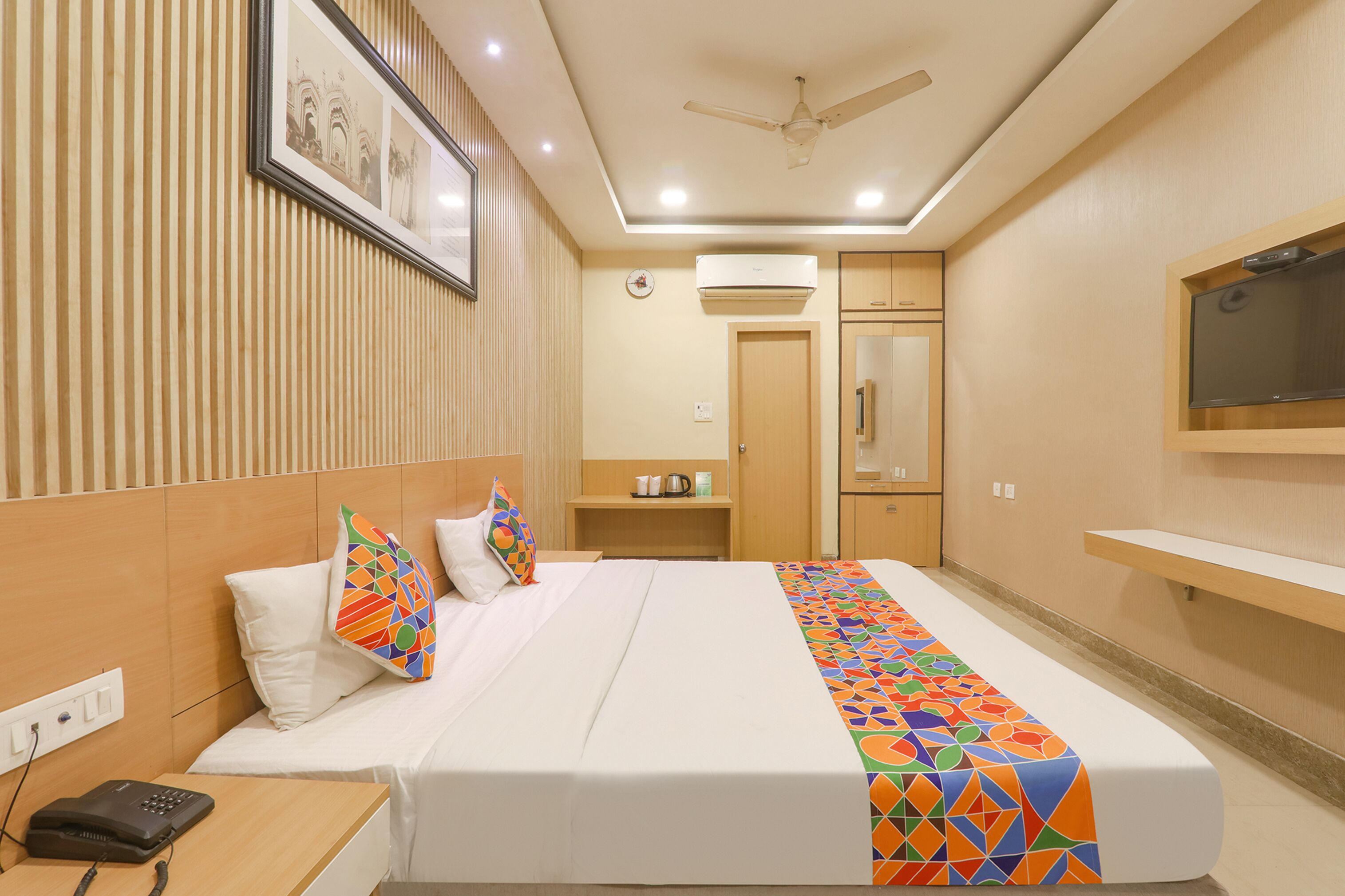 Ein Hotelzimmer mit Bett, Nachttisch, Telefon, Wand-Fernseher und Deckenventilator.