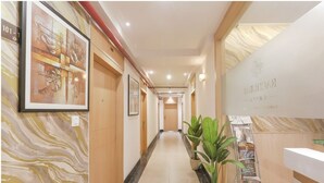 Un hall d’accueil d’hôtel avec un mur en marbre, des œuvres d’art encadrées, des plantes en pot et un comptoir de réception.