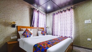 Una cama bien hecha con un edredón de diseño geométrico y colorido, un cabecero de madera y dos almohadas con un motivo geométrico multicolor.