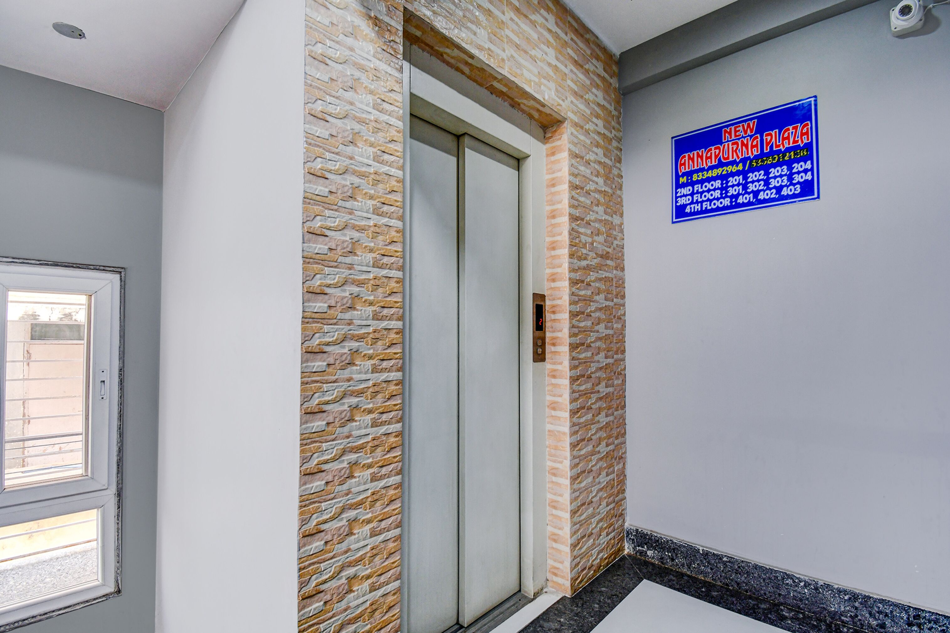 Un ascenseur dont les parois sont décorées d’un motif en pierre, avec une porte et un panneau bleu indiquant l’emplacement de New Annapurna Plaza.