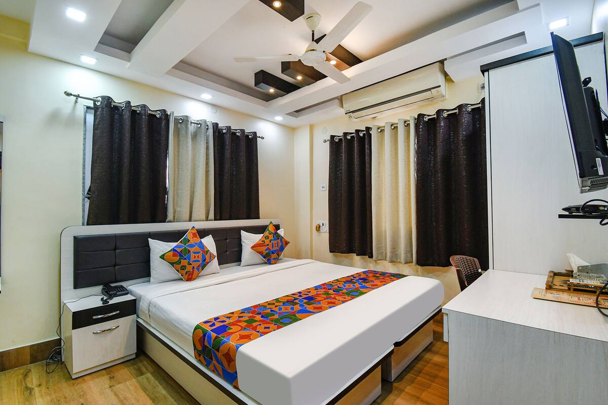 A hotel room with a bed, bedside table, nightstand, and a desk with a chair.