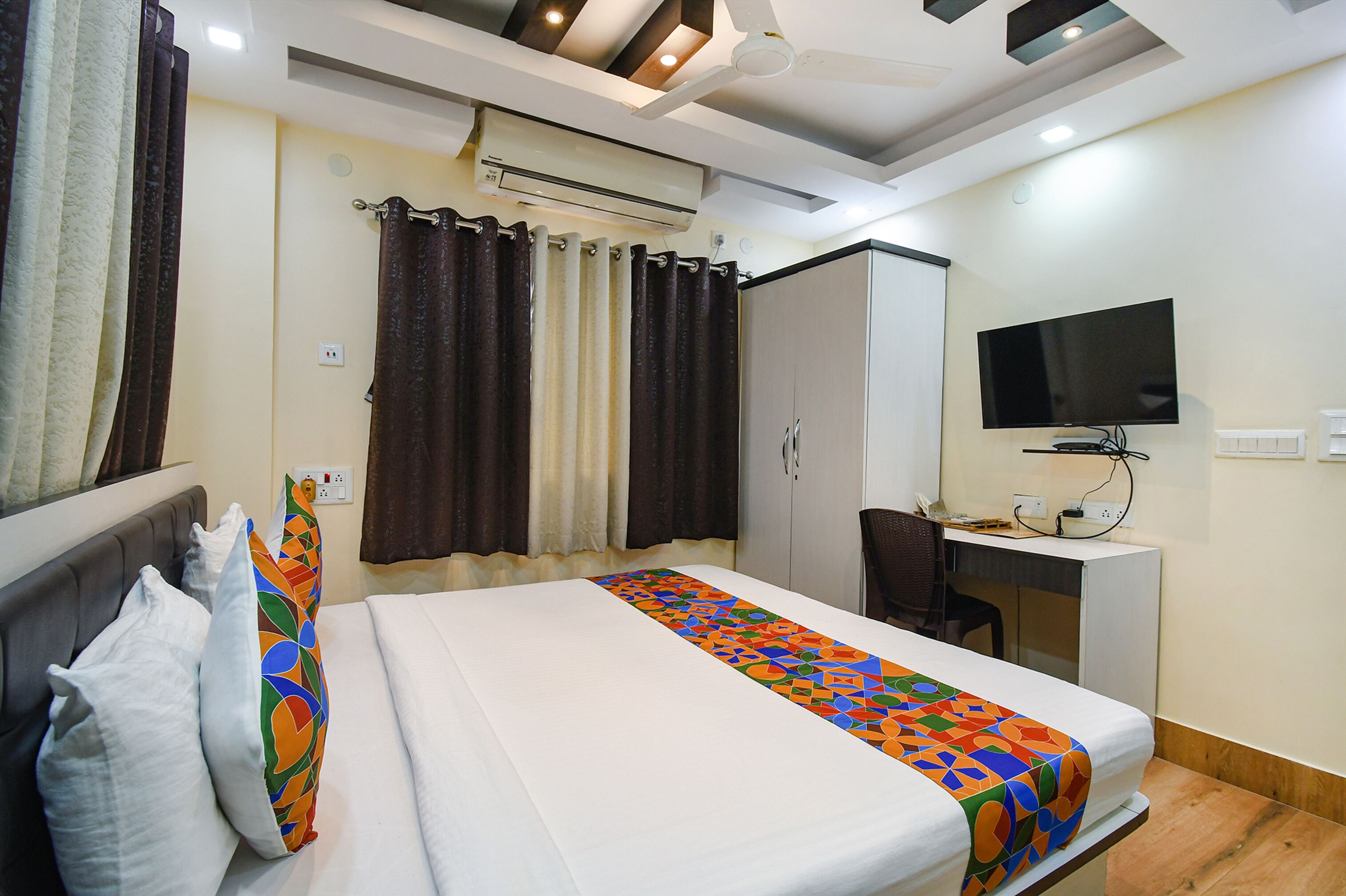 A hotel room with a bed, a desk, a chair, a television, and an air conditioning unit.