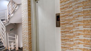 An elevator with a digital display showing the number 2, adjacent to a staircase with a white railing and a stone-textured wall. - Fabhotel New Annapurna Plaza (Barasat)