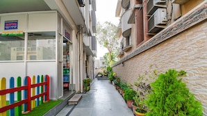 A narrow alleyway with a reception desk, colorful fence, and potted plants along the wall. - Fabhotel New Annapurna Plaza (Barasat)
