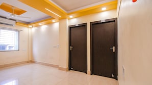 A hotel room with two dark wooden doors, a ceiling fan, recessed lighting, and a large window with blinds. - Fabhotel New Annapurna Plaza (Barasat)