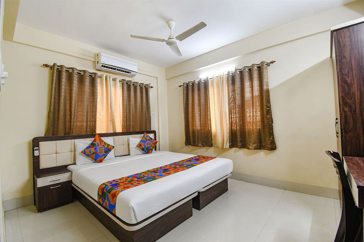 A hotel room with a bed, bedside table, nightstand, air conditioning unit, ceiling fan, and curtains.