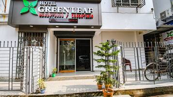 A hotel named Green Leaf with a modern facade, metal gates, and potted plants in front.
