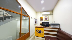 A hotel reception area with a reception desk, a brown leather couch, and a wall-mounted air conditioner. - Fabhotel Mona International (New Delhi)