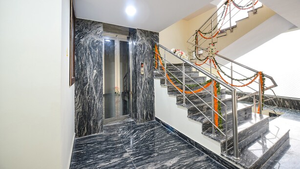A marble staircase with orange garlands, a glass elevator, and a modern interior design. - Fabhotel Mona International (New Delhi)