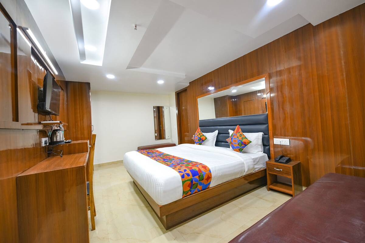 Una habitación de hotel con una cama grande, una mesita de noche, un escritorio con una silla, un espejo y un televisor.