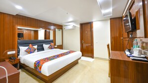 A hotel room with a large bed, wooden paneling, a television, a desk with a chair, and a bathroom door. - Fabhotel Mona International (New Delhi)