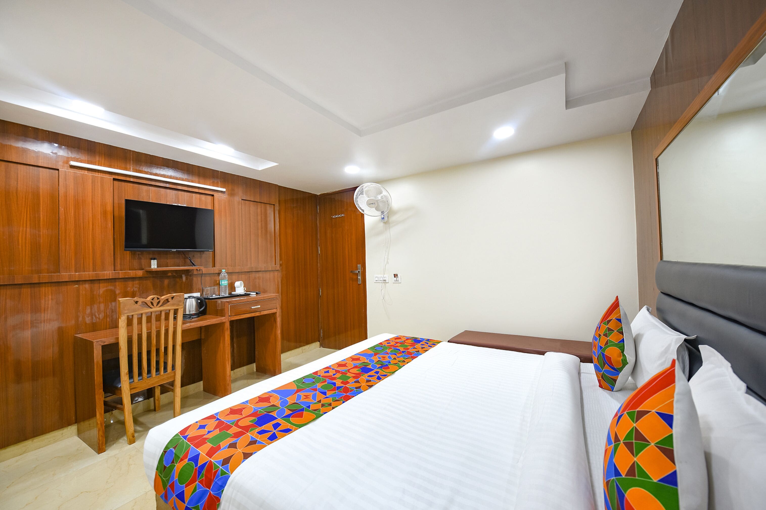 A hotel room with a bed, a desk, a television, and a ceiling fan.