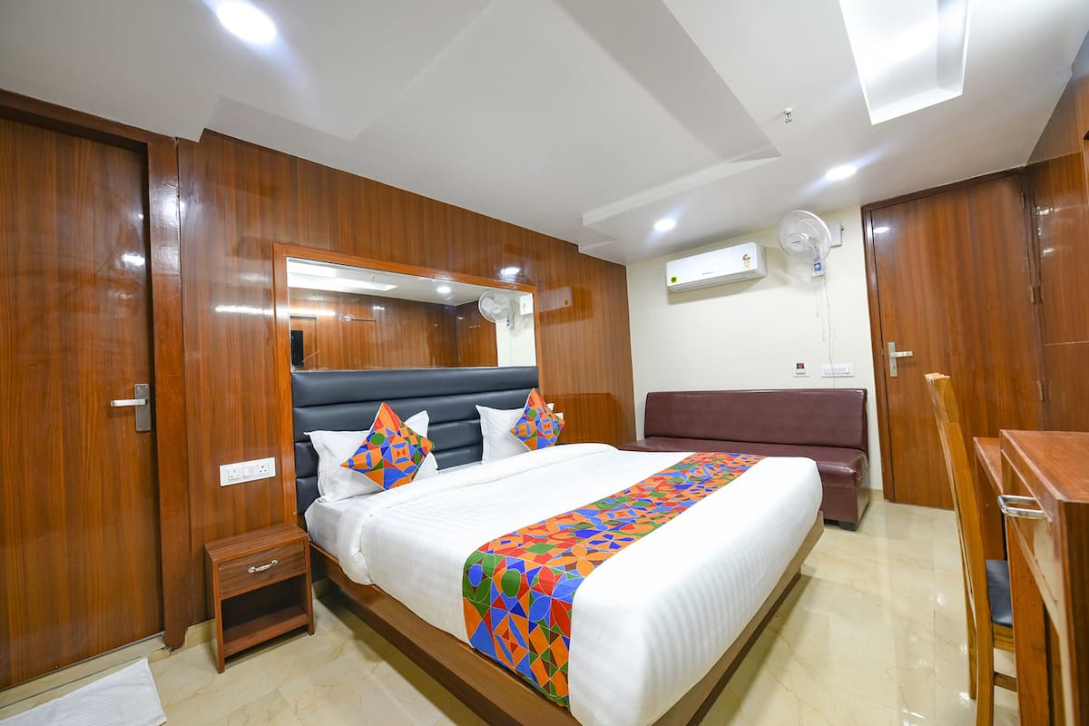 Una habitación de hotel con una cama grande, un armario de madera, una mesita de noche, una pequeña mesa y un rincón de descanso.