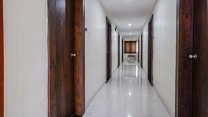 A long, narrow hallway with wooden doors on both sides and a white tiled floor. - Fabhotel V Grand (Vijayawada)