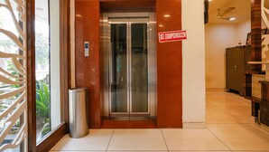 An elevator with a glass door, a metal trash bin, and a sign with a number. - Fabhotel V Grand (Vijayawada)