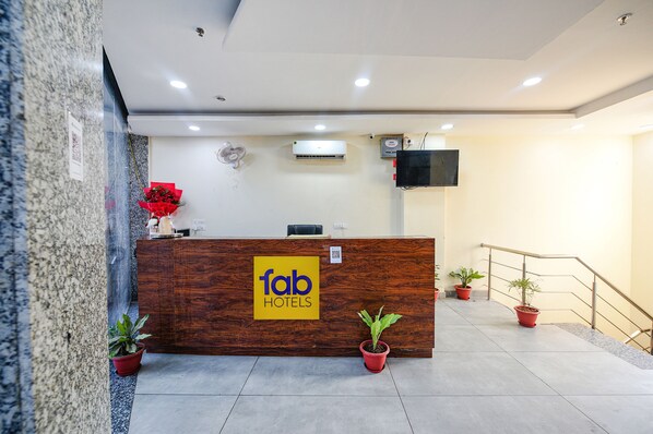 A hotel reception desk with a wooden finish, a sign reading "fab hotels", and potted plants on either side. - FabHotel HC Dream Majestic (Mohali)