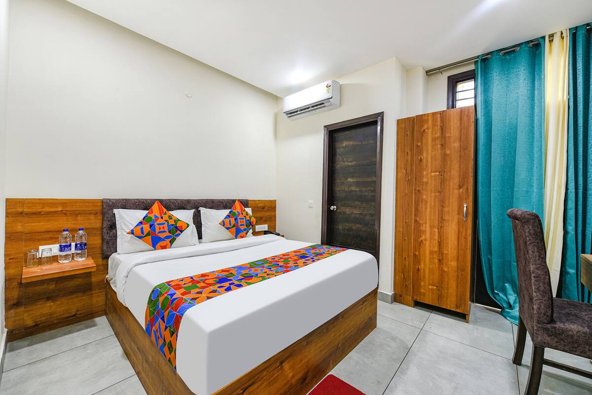 Habitació d'hotel amb llit de fusta, una tauleta de nit, una cadira, un armari i una finestra amb cortines.
