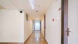 Un pasillo limpio y bien iluminado con suelo de baldosas, una puerta con un número y un detector de incendios en la pared.